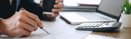 Image of a computer, calculator, and someone taking notes