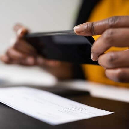 photo of two hands with a mobile phone taking a photo of a check for mobile deposit